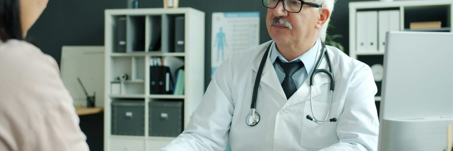 A medical examiner talking a patient through their assessment at a clinic desk A medical examiner talking a patient through their assessment at a clinic desk